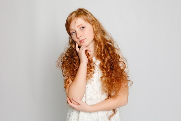 Retrato divertido de uma adorável garota ruiva em um fundo cinza. beleza, moda infantil, cosméticos, cabelos saudáveis. cabeleireiro, maquiagem, shampoo.