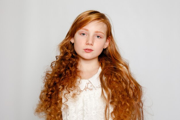 Foto retrato divertido de uma adorável garota ruiva em um fundo cinza. beleza, moda infantil, cosméticos, cabelos saudáveis. cabeleireiro, maquiagem, shampoo.