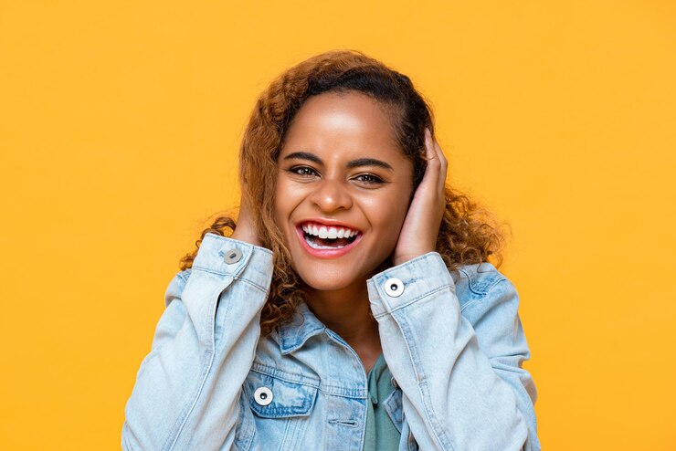 Foto retrato divertido de uma jovem afro-americana feliz rindo enquanto cobria os ouvidos com as duas mãos em fundo amarelo de estúdio isolado