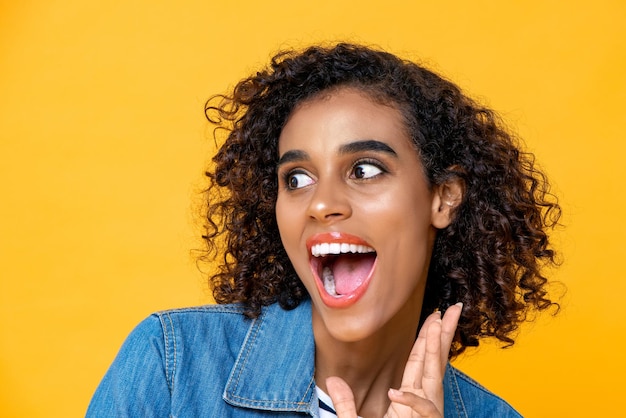 Retrato divertido de una joven afroamericana sorprendida con la boca abierta en el fondo amarillo del estudio