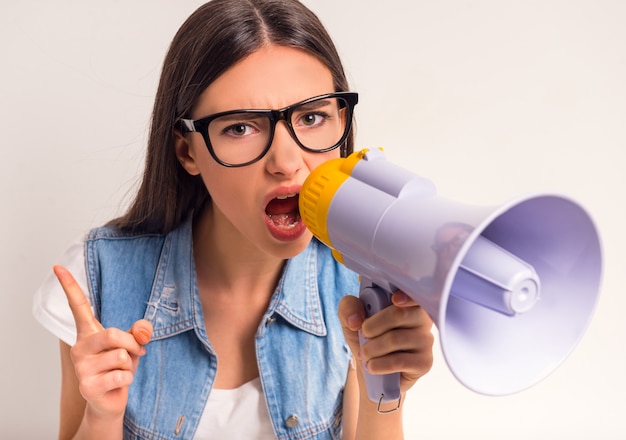 Retrato do adolescente alegre da menina, gritando em um megafone.