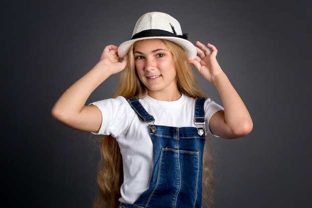 Retrato do adolescente bonito com cabelos longos no chapéu em um fundo cinzento.