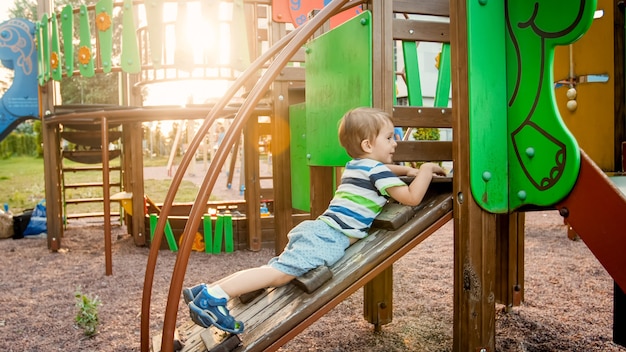 Retrato do adorável menino de 3 anos subindo em uma escada no palyground infantil no parque