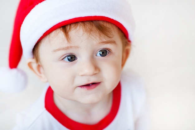 Retrato do bebê pequeno bonito de Santa nos pijamas brancos e verdes. Árvore de Natal e presentes de ano novo no