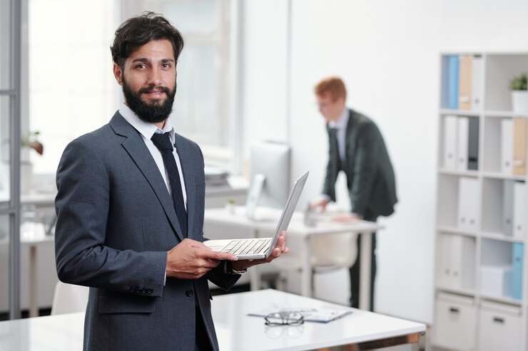Foto retrato do belo empresário barbudo segurando o laptop enquanto posa no escritório, copie o espaço da cintura para cima