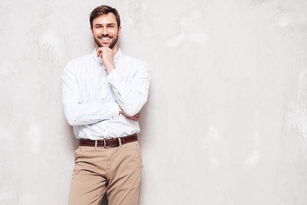 Retrato do belo modelo sorridente Sexy homem elegante vestido de camisa e calças Moda hipster masculino posando perto da parede cinza no estúdio isolado