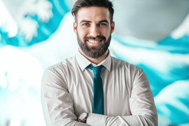 Retrato do bem sucedido empresário caucasiano barbudo com camisa e gravata em pé com os braços cruzados no escritório. no relógio de pulso. Fome suas distrações, alimente seu foco.