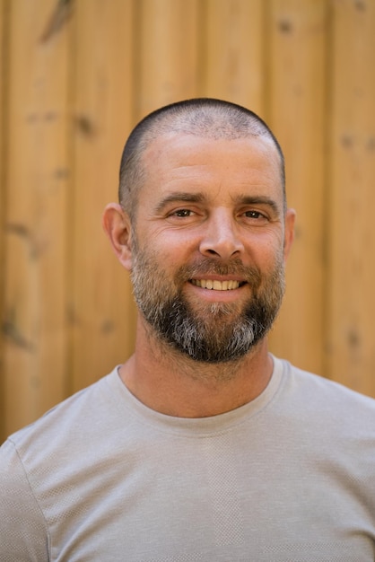 Foto retrato do bonito homem com barba sorrindo de pé contra um fundo de madeira