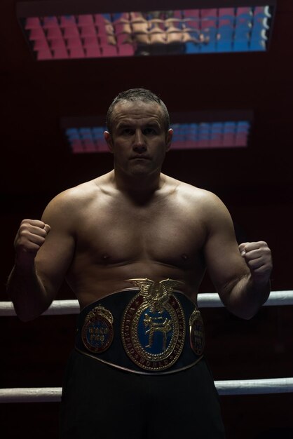 retrato do boxeador profissional musculoso com seu cinturão de campeão no ringue de treinamento