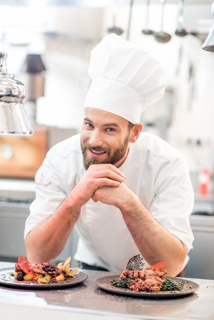 Foto retrato do chef cozinheiro de uniforme com prato delicioso preparado na cozinha do restaurante