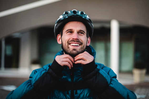 Foto retrato do ciclista prendendo seu capacete protetor. jovem feliz se prepara para as entregas em casa. retrato, ciclista, entrega em domicílio