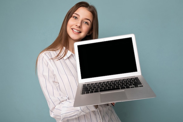 Retrato do close-up da bela jovem sorridente segurando um computador netbook, olhando para a câmera