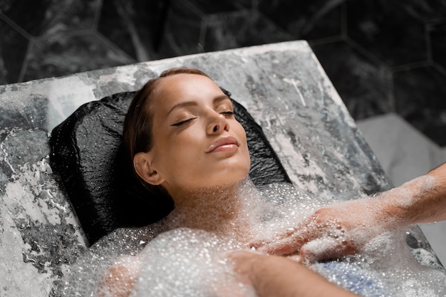 Retrato do close-up da menina em procedimentos de peeling de espuma no spa. A modelo está relaxando no hammam.