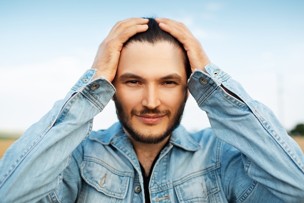 Foto retrato do close-up de jovem em jaqueta jeans, segurando as mãos na cabeça.