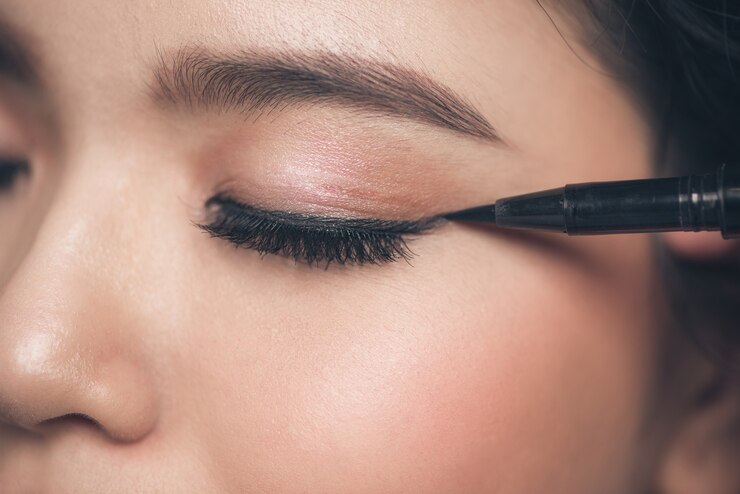 Foto retrato do close-up de menina bonita tocando o delineador preto na pálpebra com os olhos fechados.