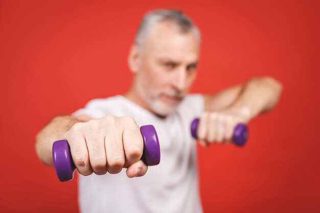 Retrato do close-up de um homem sênior que exercita com halteres.