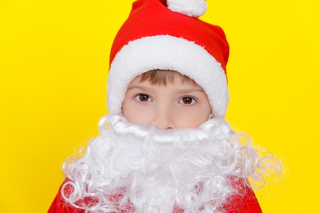 Retrato do close-up de uma criança com uma fantasia de Papai Noel de ano novo, com uma barba branca artificial.