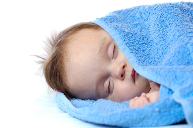 Retrato do close-up de uma menina bonitinha dorme na toalha azul sobre um fundo branco. conceito de sono saudável para o bebê.