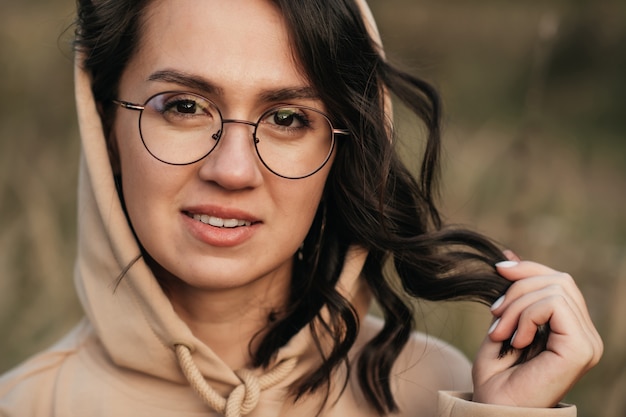 retrato do close up de uma menina morena sorridente de óculos e capuz