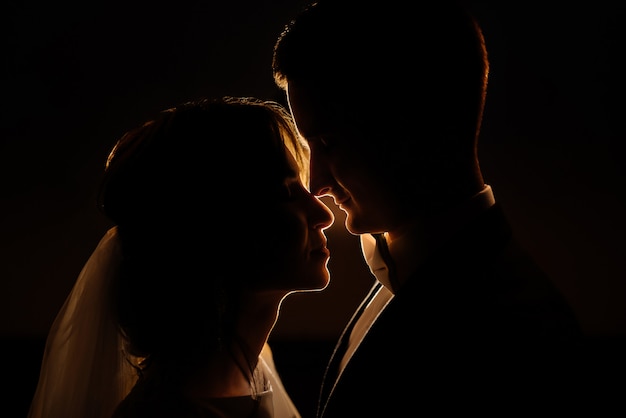 Retrato do close-up de uma silhueta de casal romântico com uma luz de fundo à noite. Idéia criativa foto de fotografia de casamento à noite. Silhueta de uma noiva e o noivo iluminado por uma luz.