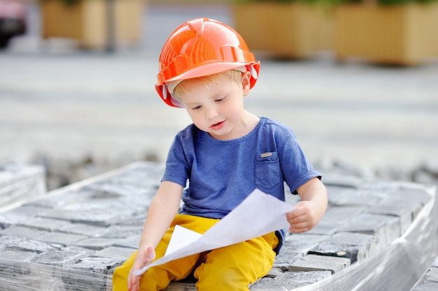 Retrato do construtor pequeno nos hardhats que lêem o desenho de construção.