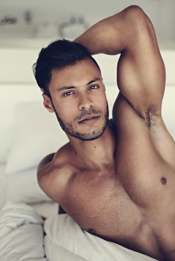 Foto retrato do corpo e acorde com um homem sexy deitado sem camisa no quarto de sua casa pela manhã relaxe o braço e os músculos com um belo modelo masculino jovem descansando em topless na cama para sensualidade