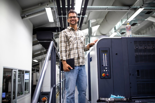 retrato do designer em pé ao lado da máquina de impressão e controlando a qualidade na fábrica de impressão