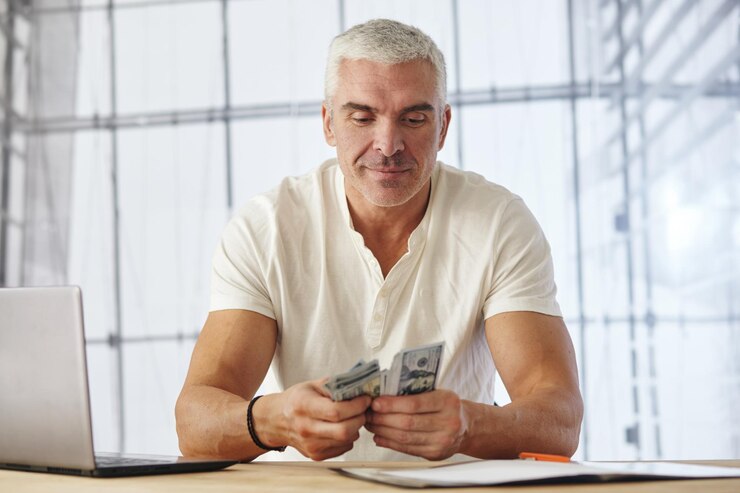 Foto retrato do empresário caucasiano atraente trabalhando no projeto na mesa de escritório com laptop, papelada. ele conta o dinheiro