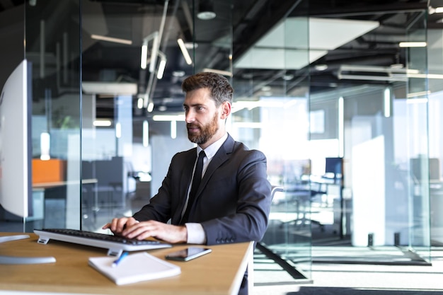 Retrato do empresário com barba homem feliz trabalhando no escritório chefe bem sucedido trabalhando no computador no escritório moderno