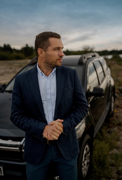 Retrato do empresário com carro clássico preto vestindo terno. Homem está parado perto de seu carro ao ar livre.