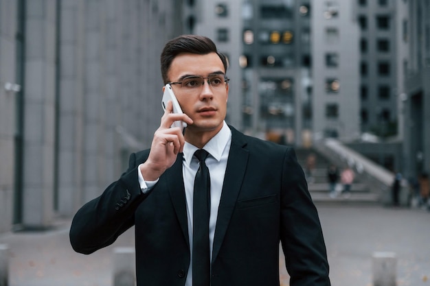 Retrato do empresário que está de terno preto e gravata está ao ar livre na cidade