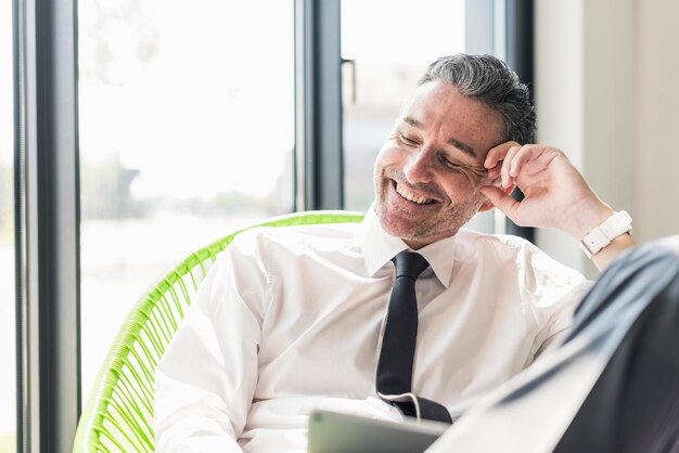 Foto retrato do empresário rindo sentado em uma poltrona em seu escritório