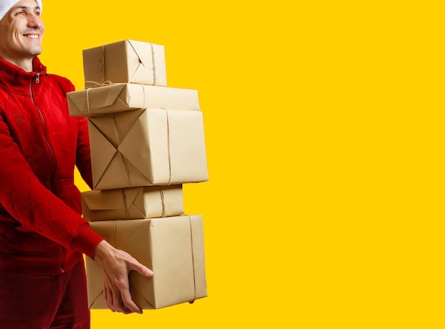 Retrato do entregador de uniforme segurando a caixa do pacote isolada sobre fundo amarelo.
