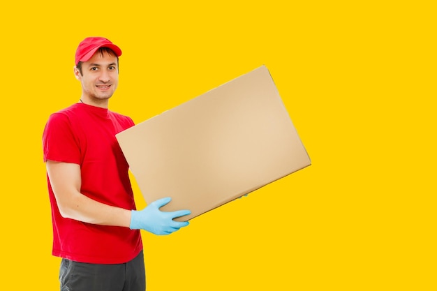 Retrato do entregador de uniforme vermelho segurando a caixa do pacote isolada sobre fundo amarelo.