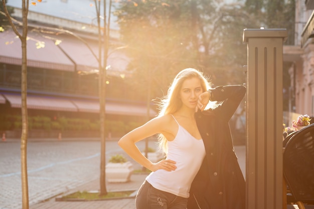 Retrato do estilo de vida da esplêndida mulher loira com exuberante cabelo encaracolado, posando com os raios do sol. Espaço para texto