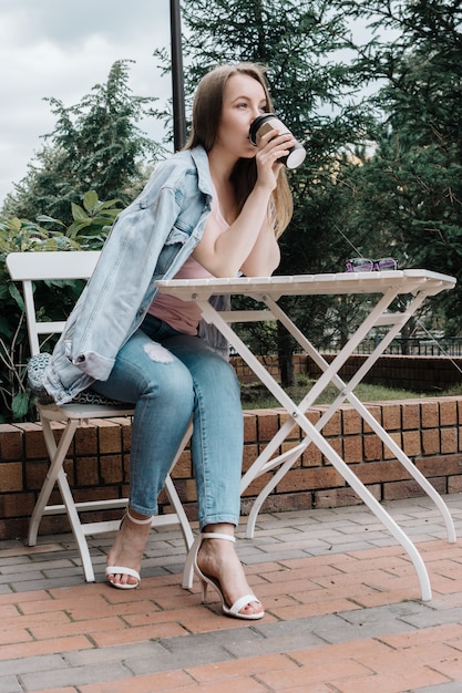 Retrato do estilo de vida da mulher branca adulta jovem segurando a xícara de café para viagem ao ar livre, foco seletivo