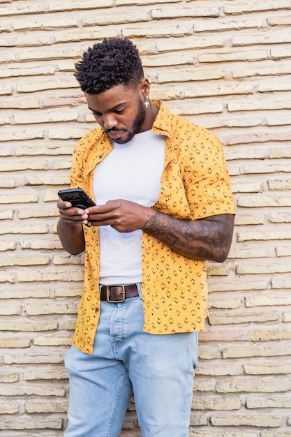 Retrato do estilo de vida de um americano bonito usando um smartphone na rua com uma parede de tijolos