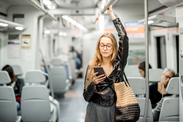 Retrato do estilo de vida de uma jovem empresária em pé com um telefone inteligente no trem moderno