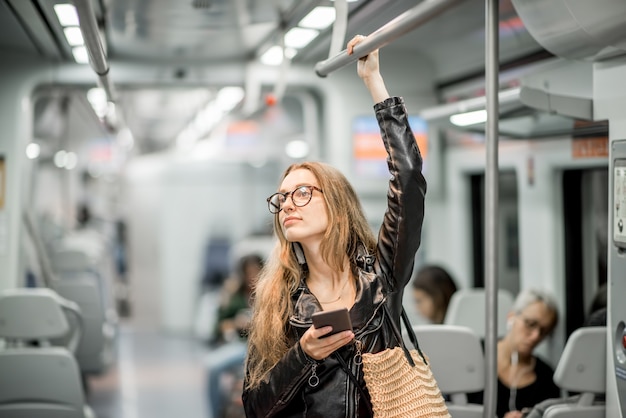 Retrato do estilo de vida de uma jovem empresária em pé com um telefone inteligente no trem moderno