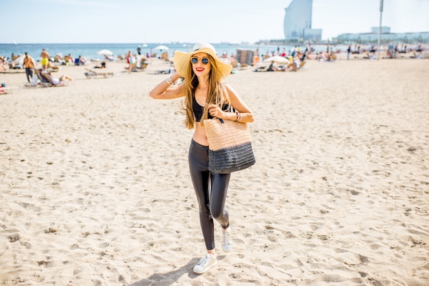 Retrato do estilo de vida de uma mulher bonita com chapéu e bolsa na praia em Barcelona