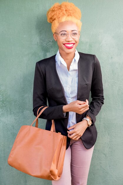 Retrato do estilo de vida de uma mulher de negócios africana em um terno casual segurando uma bolsa no fundo da parede verde.