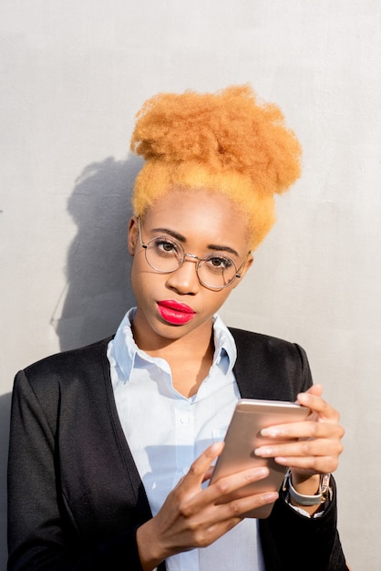Retrato do estilo de vida de uma mulher de negócios africana em um terno casual usando telefone inteligente no fundo da parede cinza