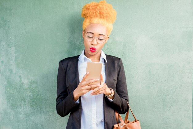 Retrato do estilo de vida de uma mulher de negócios africana em um terno casual usando telefone inteligente no fundo da parede verde.