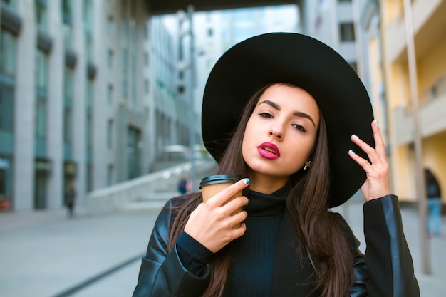 Retrato do estilo de vida do modelo Moreno elegante com uma xícara de café, usando um chapéu de aba larga. Café para levar conceito