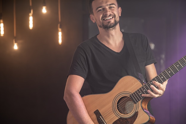 Retrato do guitarrista sorridente em t-shirt preta tocando violão.