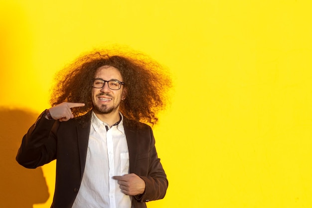 Retrato do homem de negócios cabelos longos e óculos apontando os dentes e sorriso sobre fundo amarelo