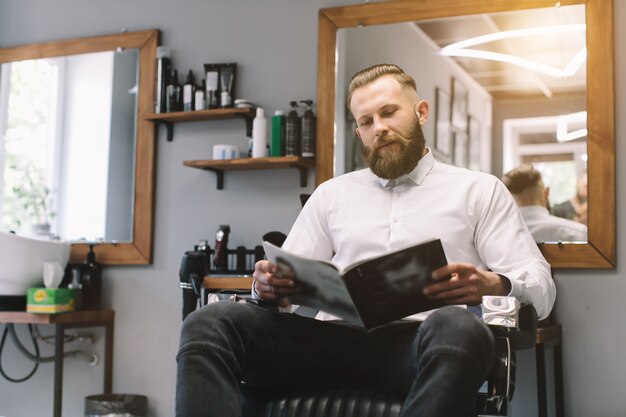 Retrato do homem farpado considerável com penteado elegante e barba na barbearia.