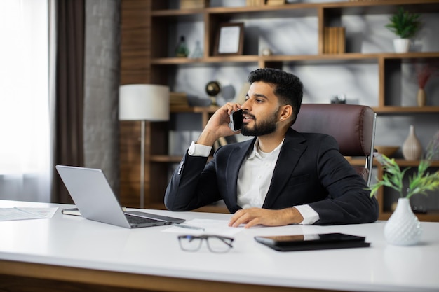 Retrato do homem sentado à mesa na cadeira, tendo telefonema com parceiros de negócios no novo escritório moderno