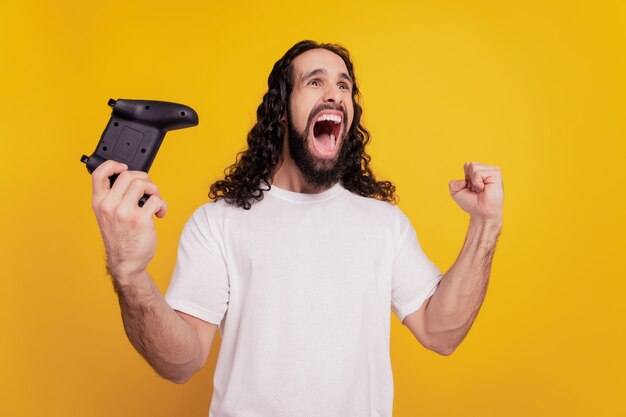 Retrato do jogador vencedor segurando gamepad para jogar videogame em fundo amarelo