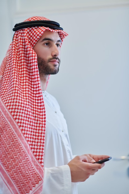 Retrato do jovem empresário muçulmano usando telefone celular. Menino árabe bem-sucedido em roupas tradicionais que representam tecnologia